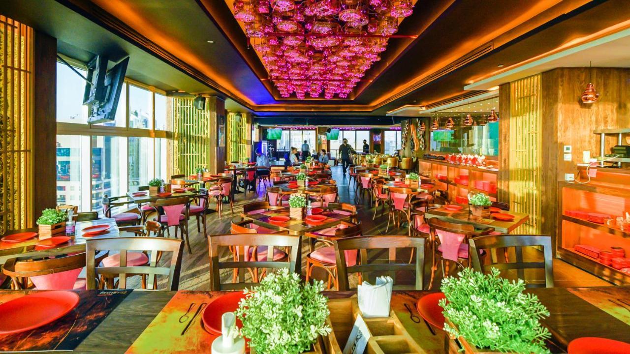 Stella Di Mare Dubai Marina Hotel Exterior foto The photo depicts a vibrant restaurant interior featuring a modern and stylish design. The space has a warm ambiance with wooden furniture and colorful table settings, including red plates and greenery centerpieces. The ceiling is adorned with a stri