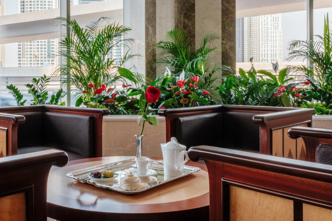Stella Di Mare Dubai Marina Hotel Exterior foto The photo shows an inviting indoor setting, likely from a restaurant or hotel lobby. In the center, there is a wooden table with a tray that holds a white teapot, a small vase with a single red rose, and some snacks or pastries. Surrounding the table